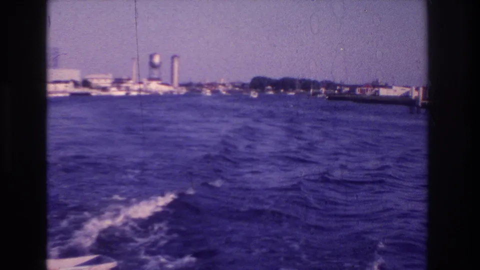 1968 Ocean City, New Jersey home-movie frame showing rippled water, boat wake, docks, and a distant water tower.