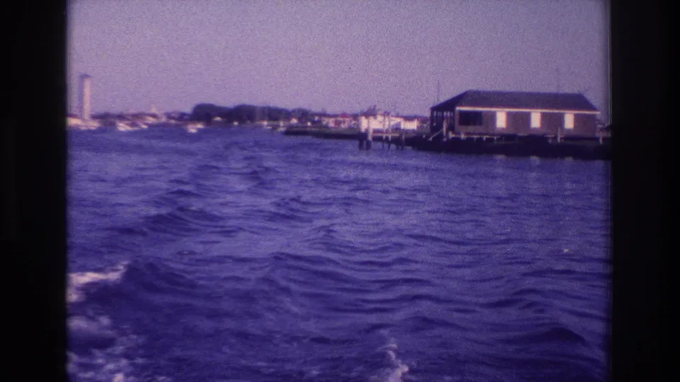 1968 Ocean City, New Jersey home-movie frame showing choppy bay water from a boat, with shoreline buildings and a small structure on pilings.