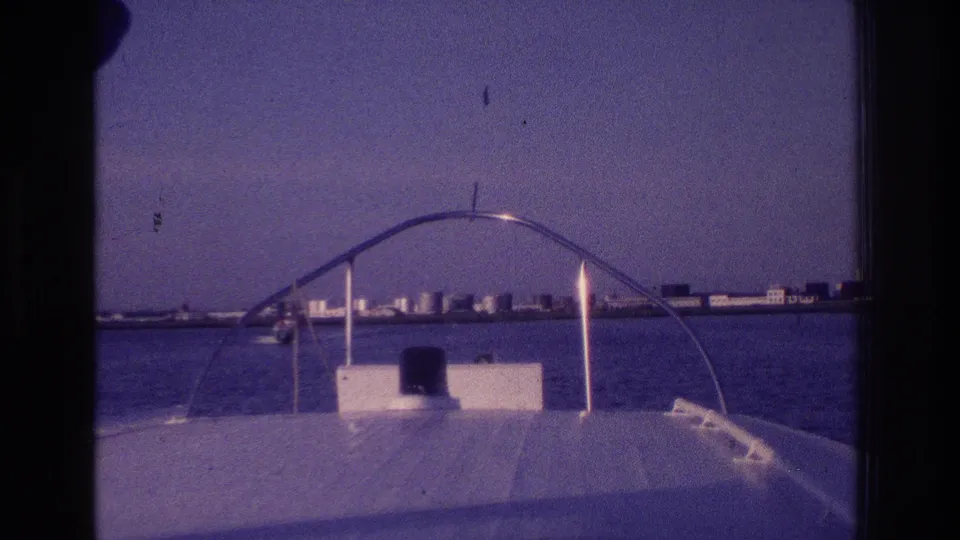 1968 Ocean City, New Jersey home-movie frame with a motorboat bow, curved metal rail, and low buildings beyond the bay.