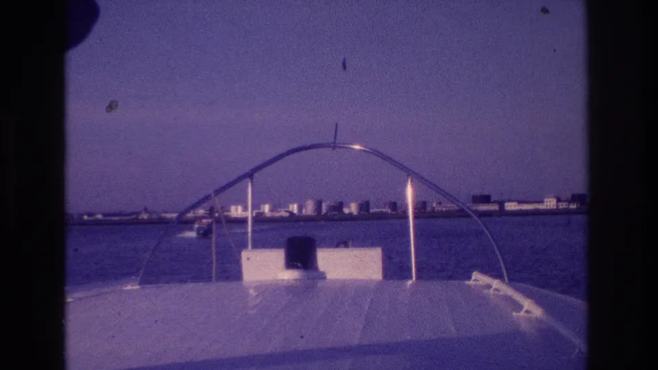 1968 Ocean City, New Jersey 8mm frame from a motorboat bow, showing a curved rail, calm water, and low shoreline buildings.