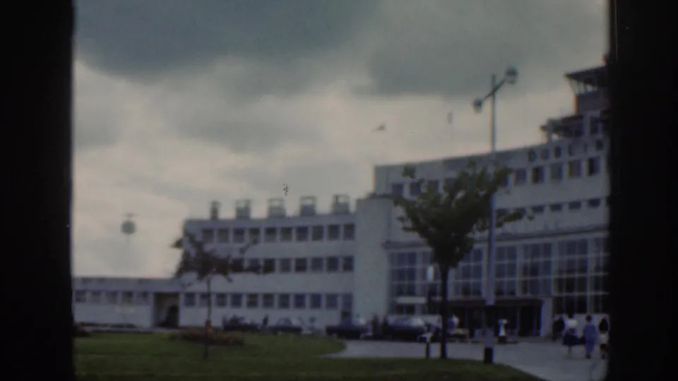 Dublin Airport terminal exterior in 1961 with modernist buildings, lawn, walkway, lamp posts, and small groups of people.