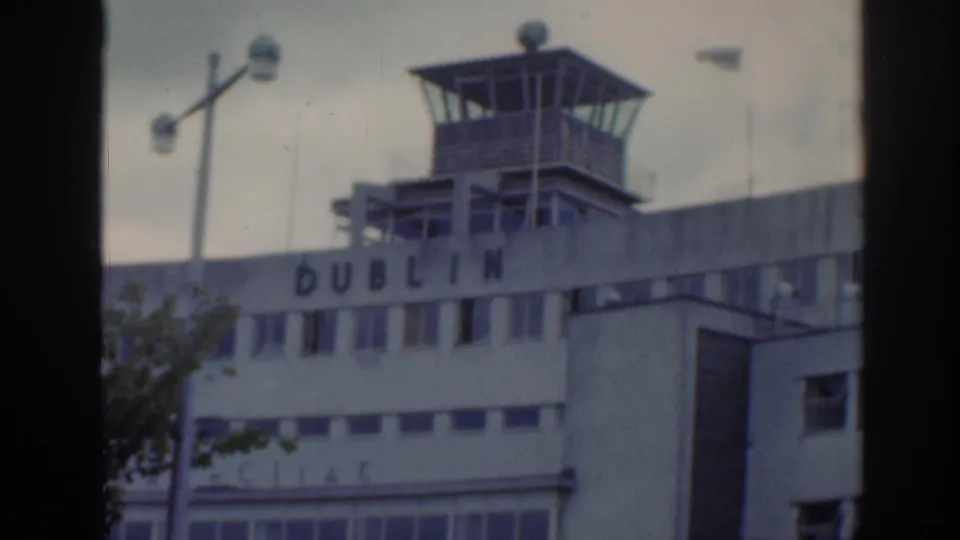 1961 Dublin Airport tower and facade lettering seen in a soft handheld 8mm frame with cloudy sky above.