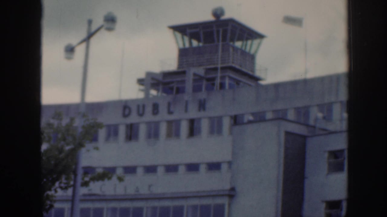 1961 Dublin home-movie frame showing an airport building with control tower, partial Dublin lettering, and a window-like dark border.