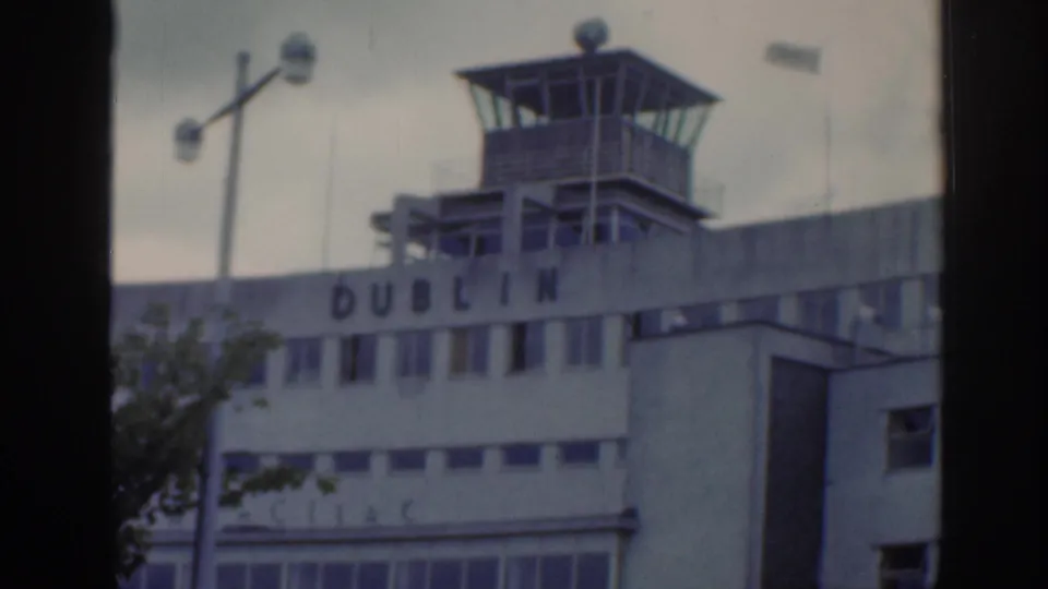1961 Dublin home-movie frame showing an airport building with control tower, partial Dublin lettering, and a window-like dark border.
