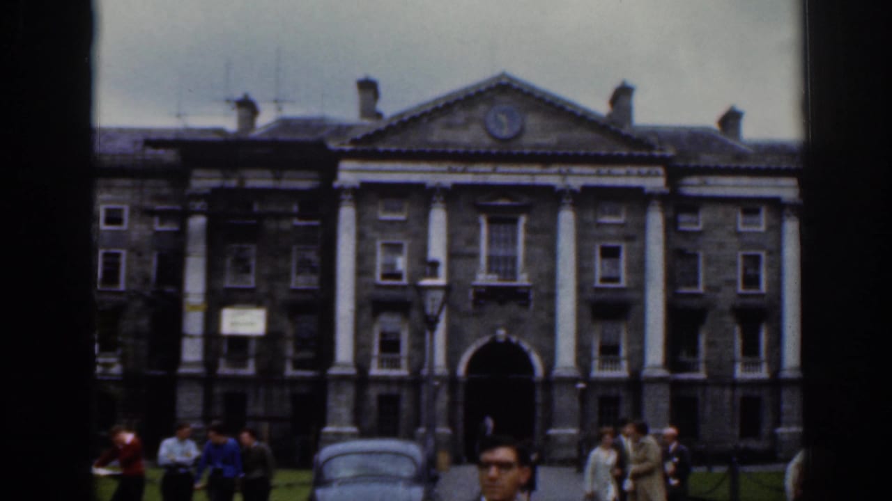 Dublin 1961 frame of a large classical stone building with columns, a clock pediment, and pedestrians gathered in front.