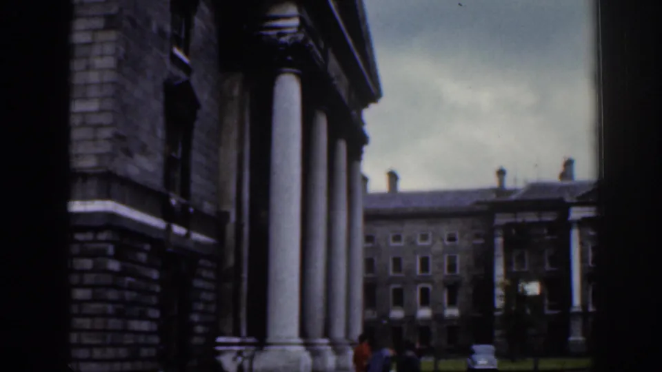 1961 Dublin home-movie view of tall white columns beside a courtyard, with a stone building and small pedestrians in the distance.