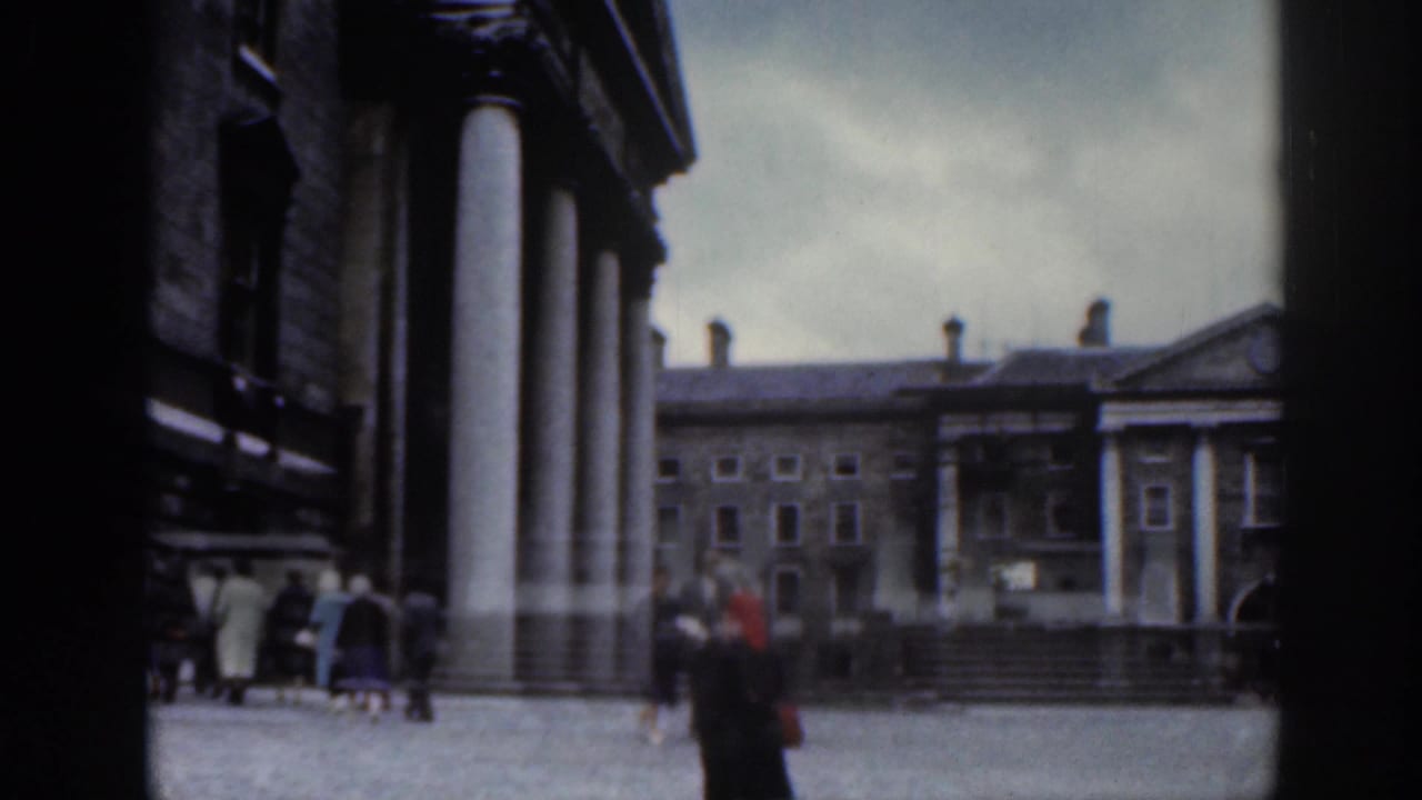 Pedestrians cross a cobbled courtyard between stone buildings with columns.