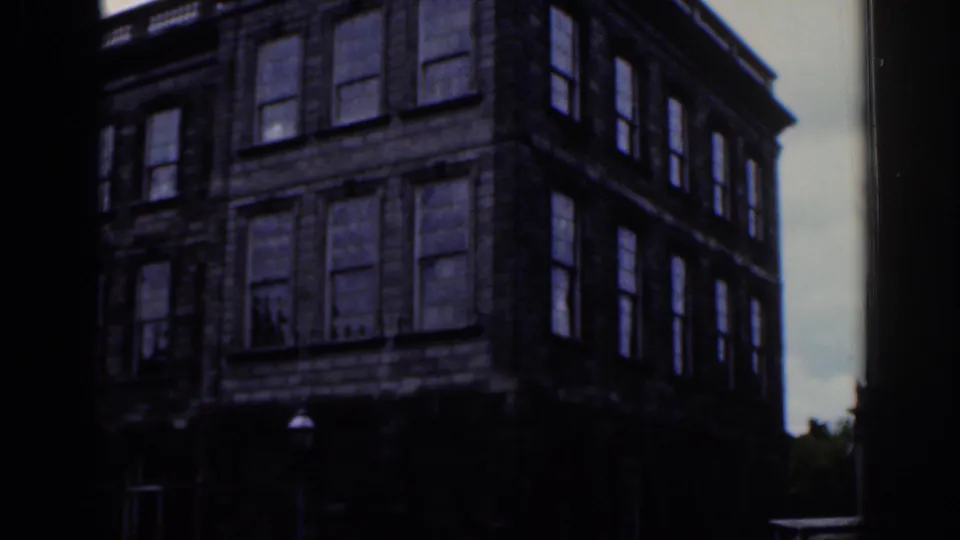 1961 Dublin home-movie shot of a multi-story stone building with rows of windows, partly obscured by dark film or doorway edges.