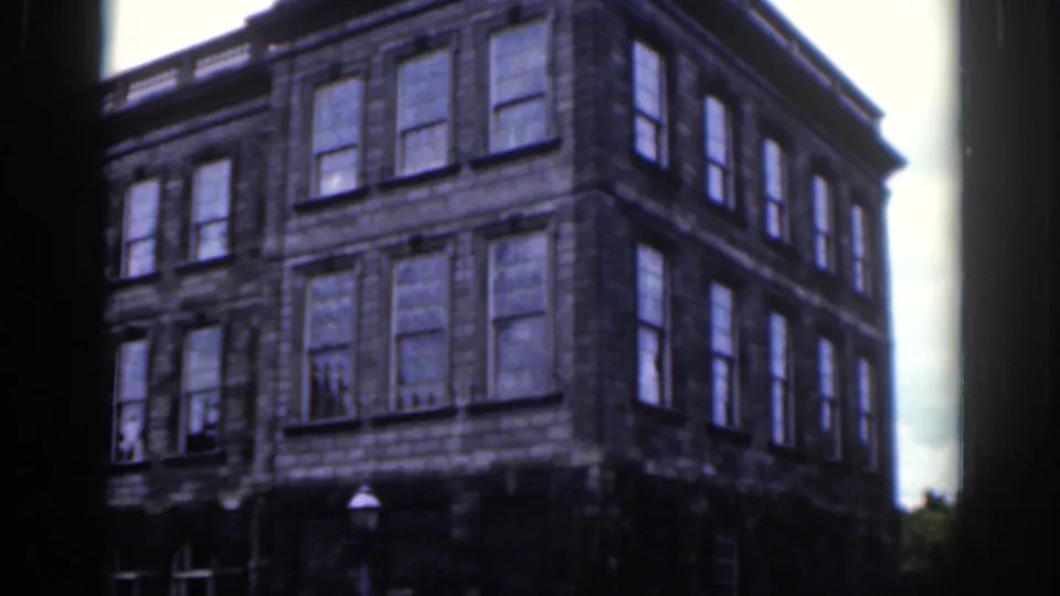 1961 Dublin view of a stone building facade with tall windows, filmed in soft 8mm color from a nearby public space.