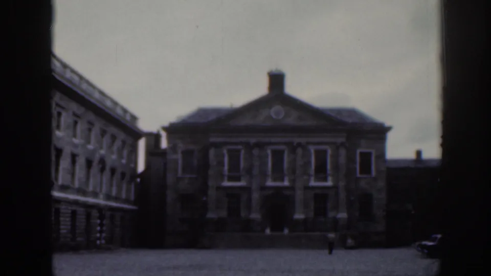 1961 Dublin home-movie frame showing a grand stone facade and sparse pedestrian activity in a public square.