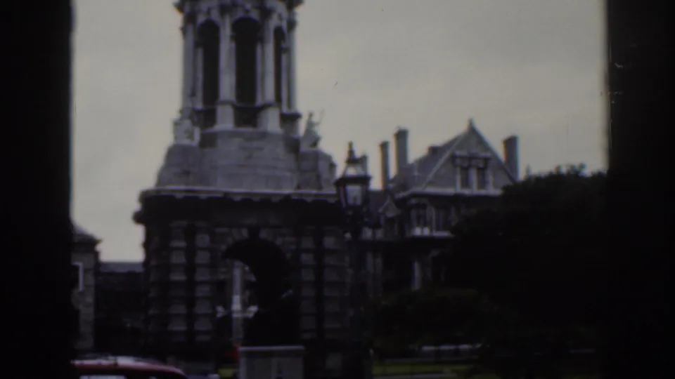 1961 Dublin frame showing a stone arched gateway or tower with nearby historic-looking buildings and dark film edges.