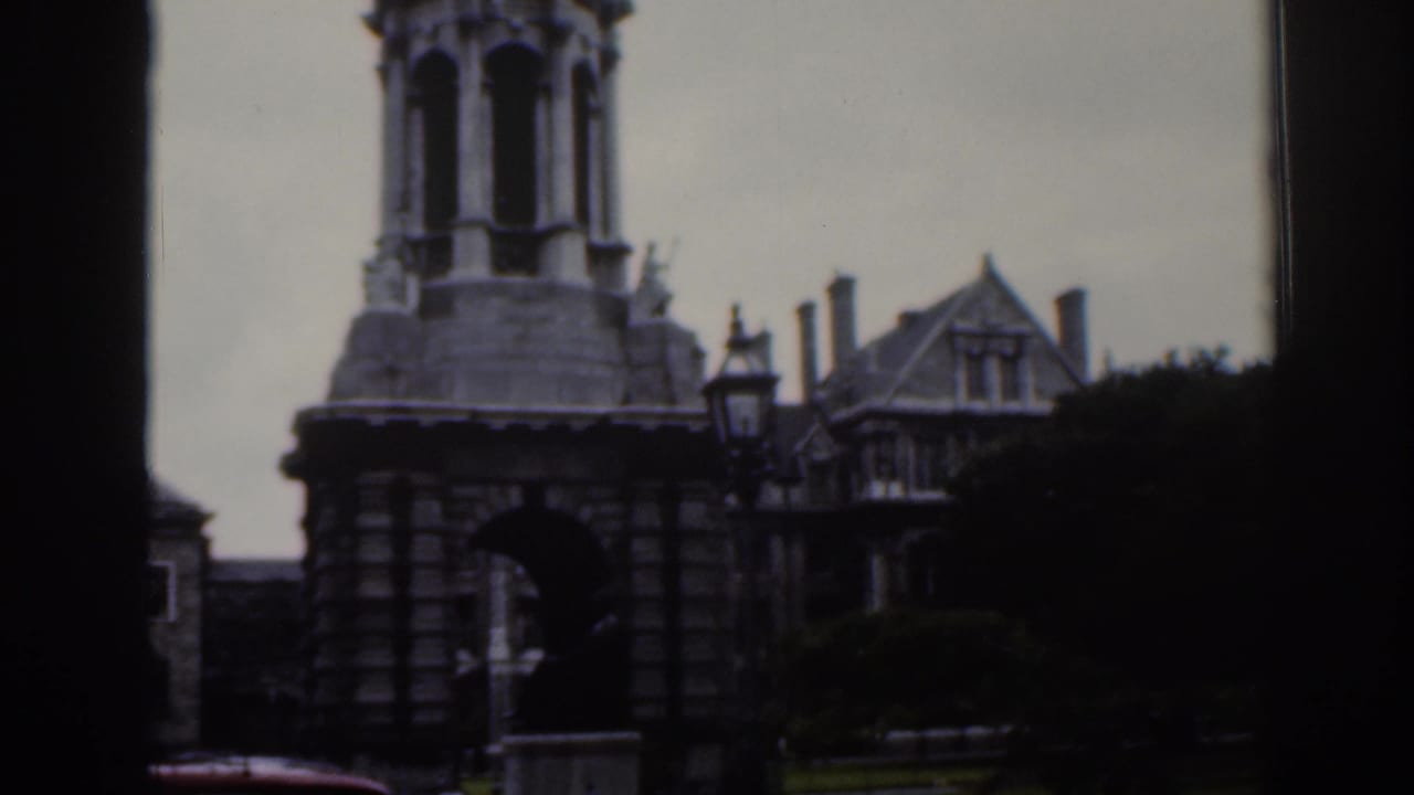 1961 Dublin home-movie frame showing a stone tower with arched openings beside gabled buildings and a street lamp.
