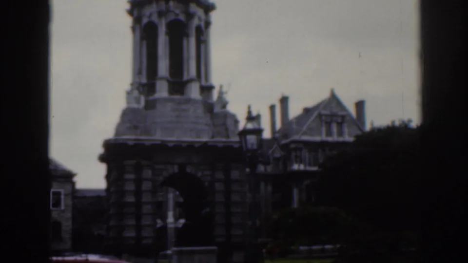 1961 Dublin frame with a stone tower, arched passage, street lamp, and adjoining gabled building in soft focus.