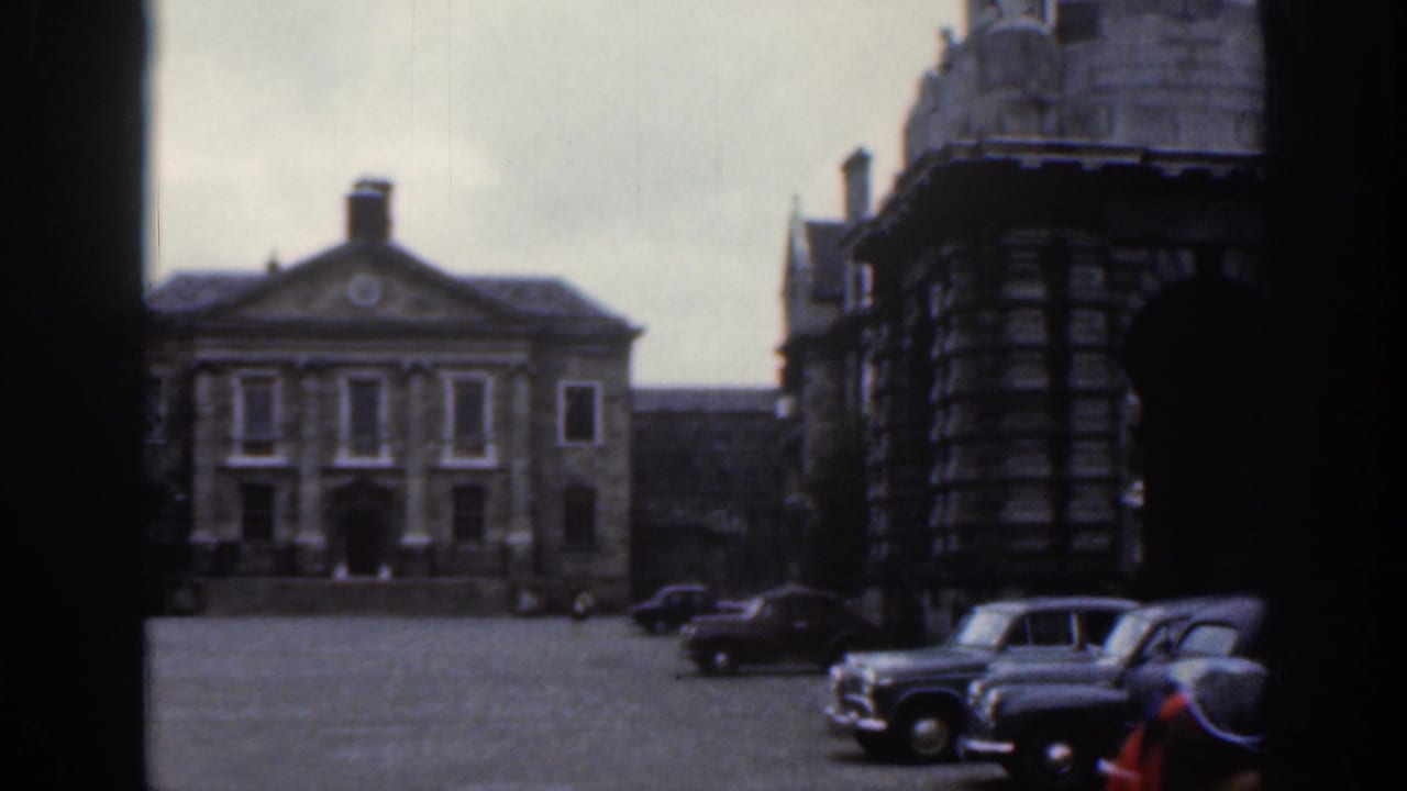 1961 Dublin courtyard view with several parked vintage cars, a classical stone facade, cobbled or paved ground, and surrounding dark masonry.