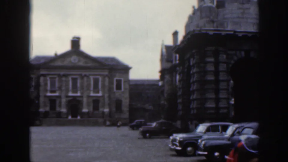 1961 Dublin courtyard view with several parked vintage cars, a classical stone facade, cobbled or paved ground, and surrounding dark masonry.