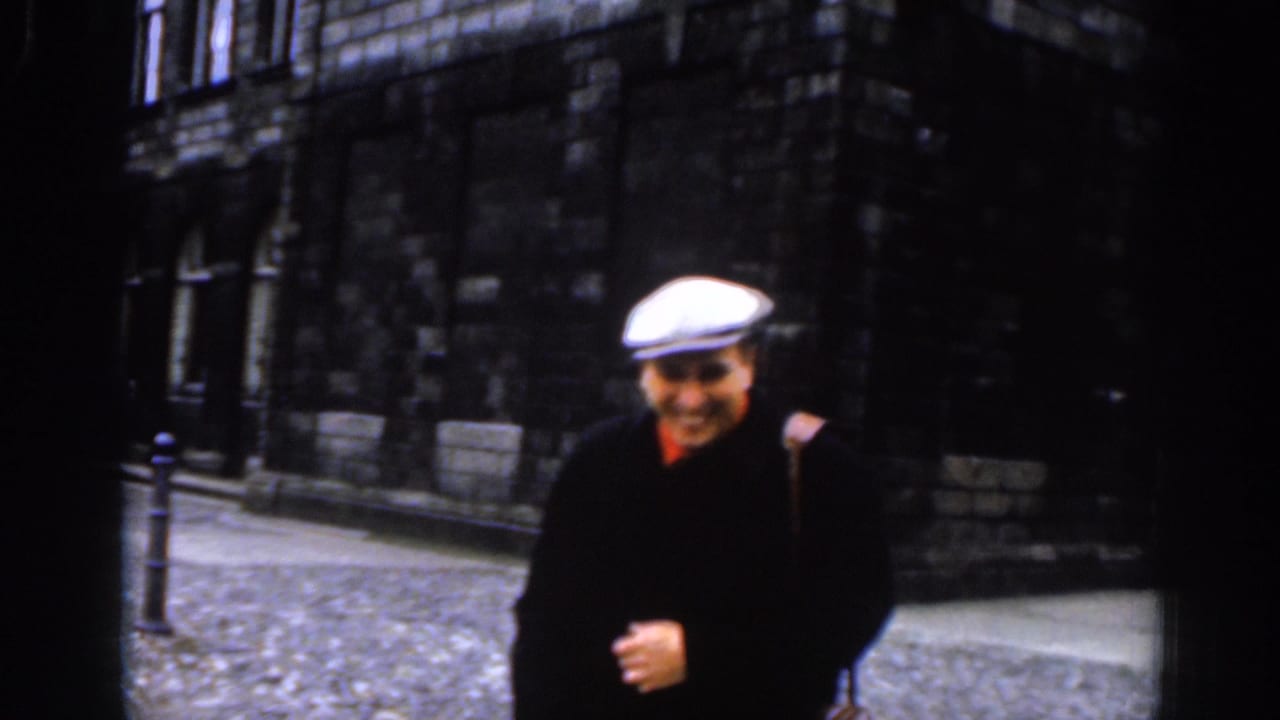The man in a flat cap and dark coat looks toward the camera on a Dublin cobblestone street in the 1961 home-movie footage.