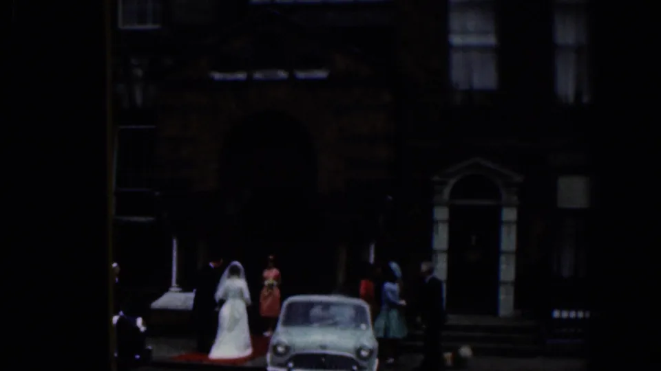 1961 Dublin church exterior with a bride in a white gown, wedding guests, and a small period car near the entrance.