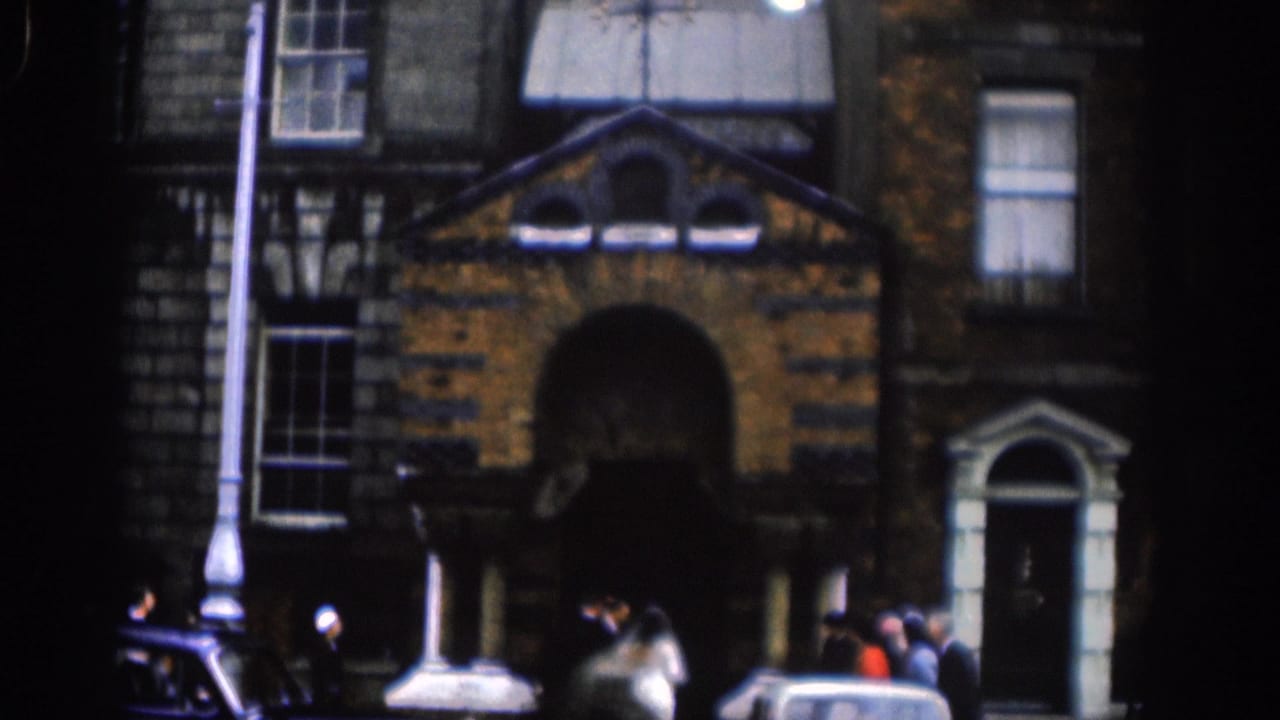 Closer 1961 Dublin view of a brick church exterior, arched doorway, tall windows, guests, and cars near the curb.