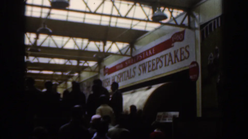Dublin 1961 interior frame with silhouetted people beneath skylights and a large Irish Hospitals Sweepstakes banner.