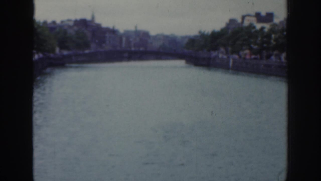 Wide river view with a bridge in the distance and tree-lined stone banks.
