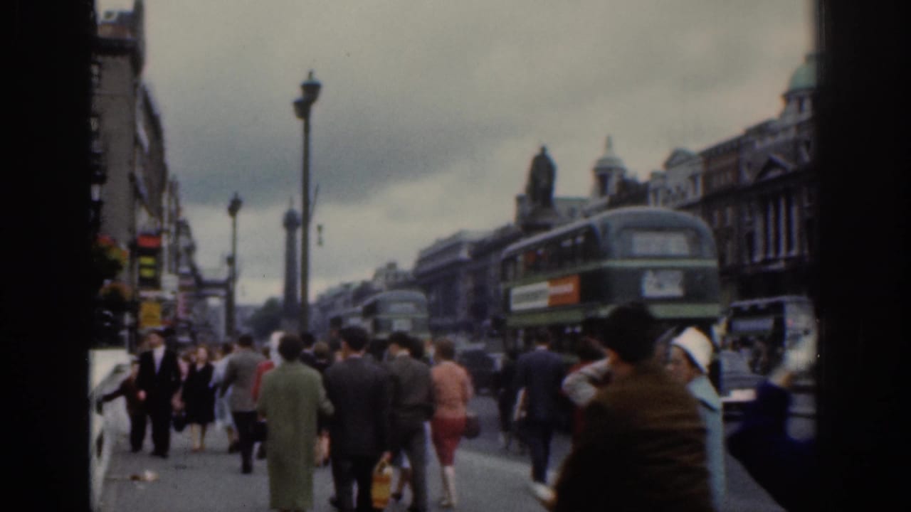 Dublin city sidewalk scene with walking pedestrians, a green double-decker bus, traffic, street lamps, and commercial buildings.