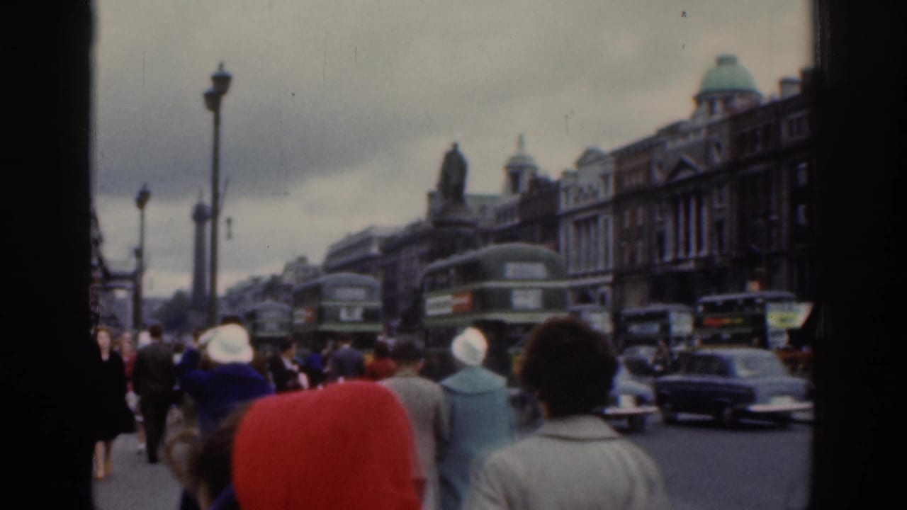 Dublin street scene with foreground pedestrians, green double-decker buses, classic cars, ornate lamp posts, a statue, and dense buildings.