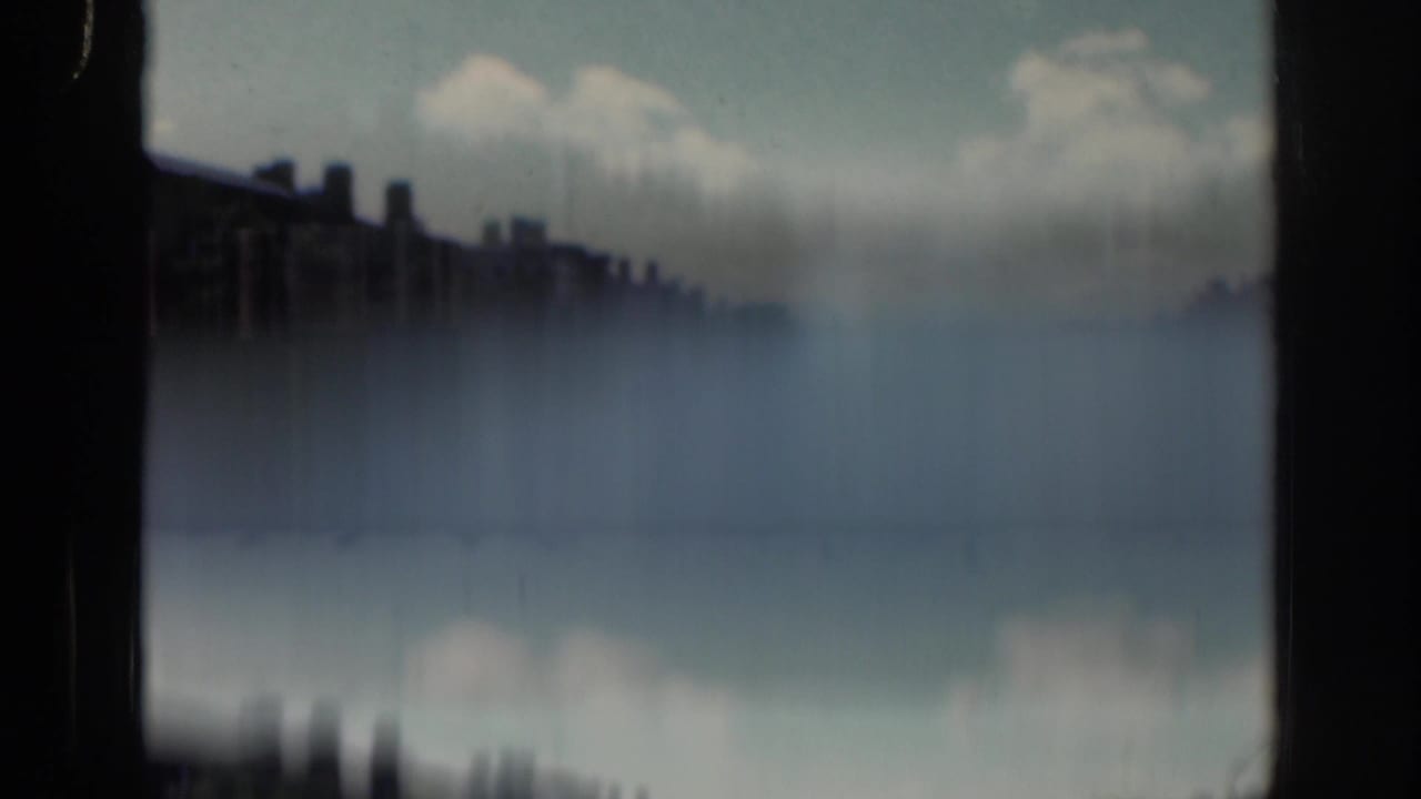 A soft final 1961 Dublin frame appears to show a riverside or bridge view, with dark building silhouettes, pale water, clouds, and strong film blur.