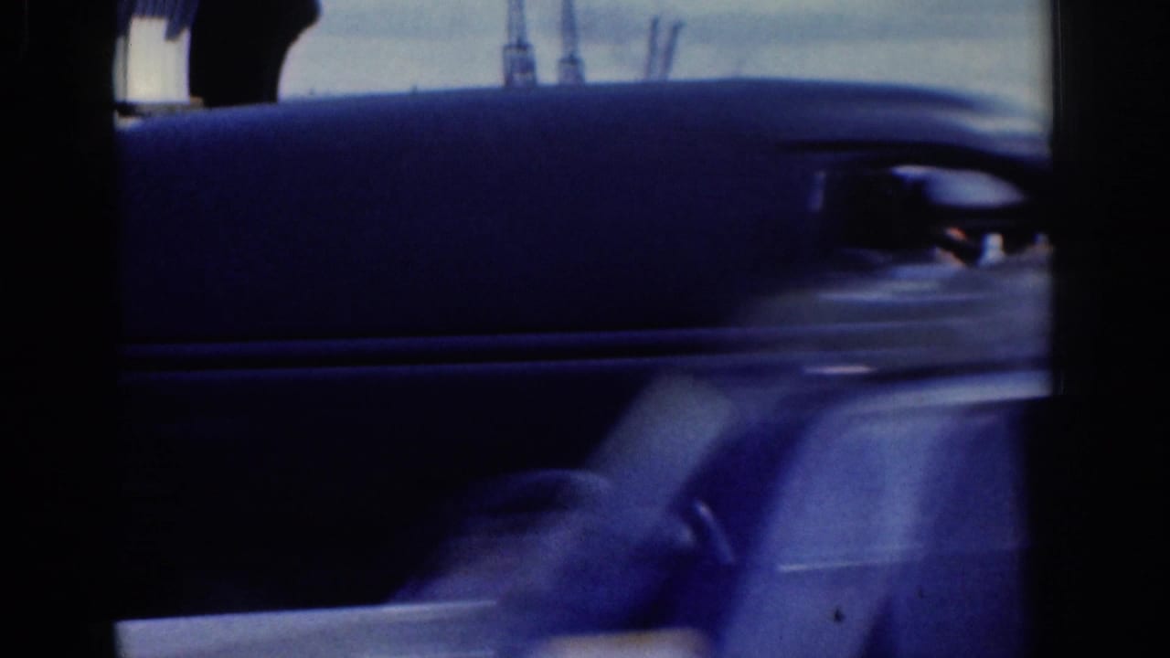 Mid-century automobile passes close to camera, partially obscuring a cyclist and street background in Dublin footage.