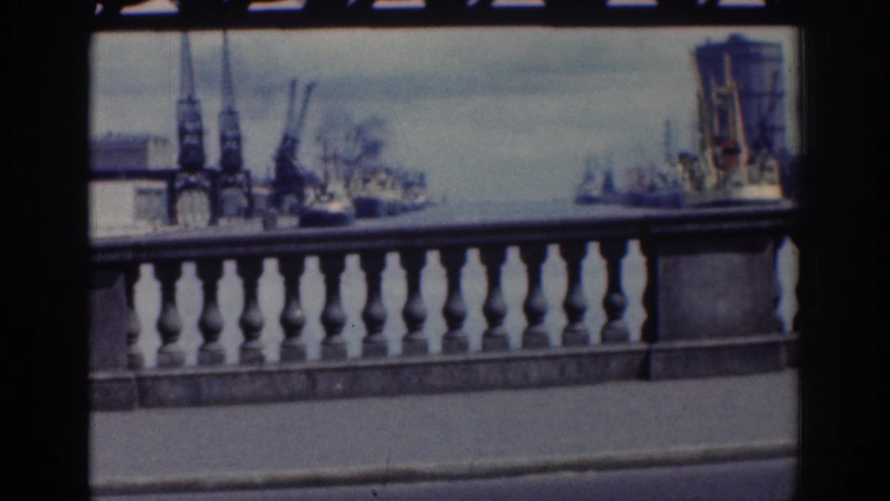 Dublin waterfront view from the road, showing a stone balustrade, cranes, and ships across the harbor in soft 8mm color.