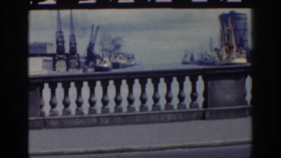 Dublin waterfront view from the road, showing a stone balustrade, cranes, and ships across the harbor in soft 8mm color.