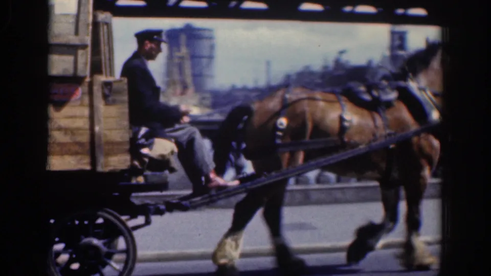 1961 Dublin footage shows a brown horse pulling a crate-loaded wagon as a uniformed driver sits at the reins on a city street.