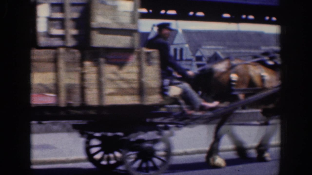 Horse and crate wagon passing across the frame on a city street.