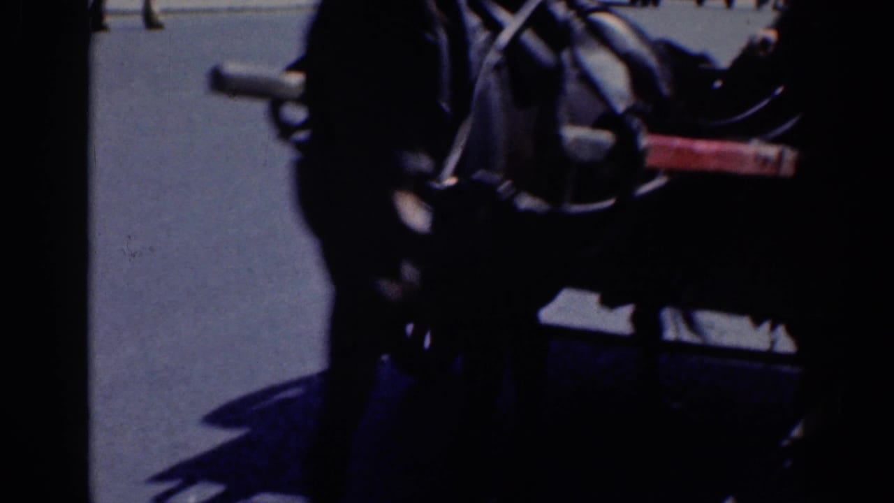 Dark 8mm frame of a horse-drawn carriage on a Dublin street, with pavement and distant pedestrians visible.