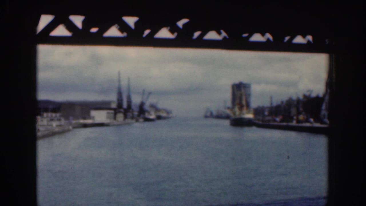 Dublin, 1961, seen from a bridge-framed viewpoint across a river or canal with cranes, dockside buildings, and a large vessel or structure to the right.
