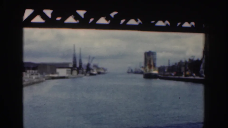 Dublin, 1961, seen from a bridge-framed viewpoint across a river or canal with cranes, dockside buildings, and a large vessel or structure to the right.
