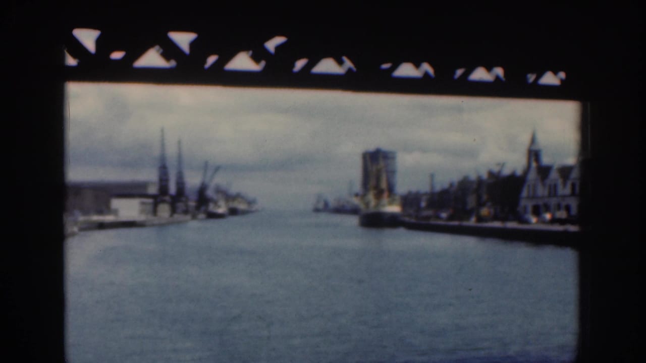 1961 Dublin riverfront framed by a bridge, with cranes and low port buildings on the left and a large ship or tall structure on the right bank.