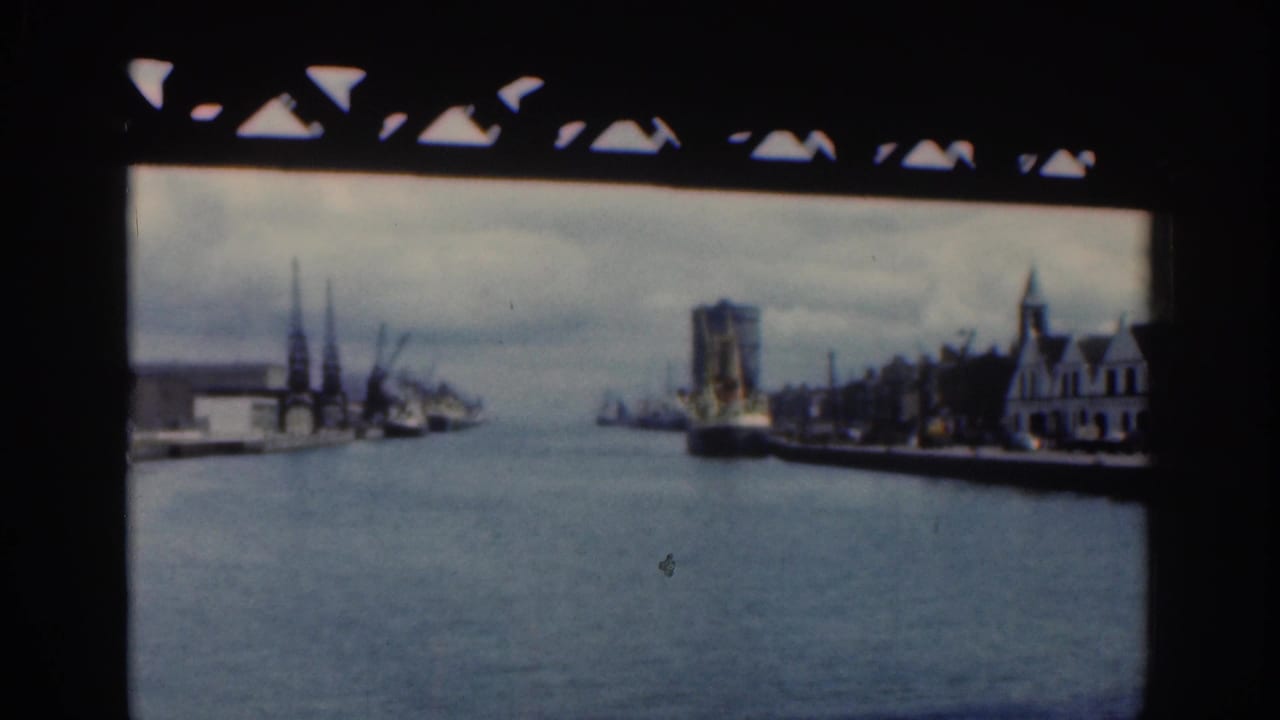 1961 Dublin waterfront or harbor view with water, distant buildings, and dark film-frame borders from home-movie footage.