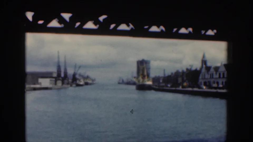 1961 Dublin waterfront or harbor view with water, distant buildings, and dark film-frame borders from home-movie footage.