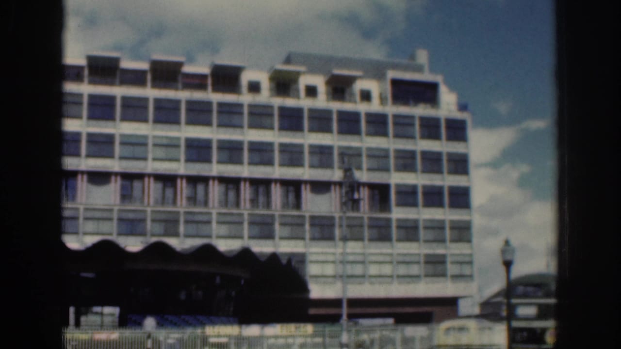 Large modernist multi-story building in Dublin, 1961, viewed from a street-level moving home-movie perspective.