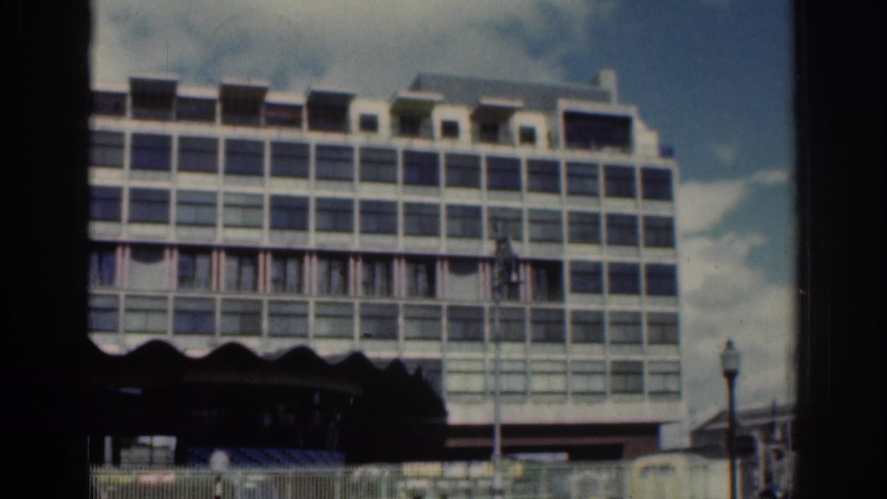 1961 Dublin street view showing a large gridded building facade, dark awning line, and street lamps from 8mm footage.