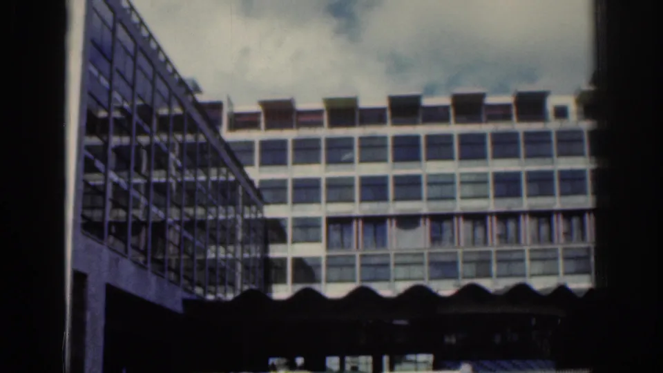 1961 Dublin home-movie frame showing a modern grid-window building with a darker glass-sided structure at left.