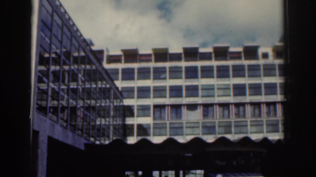 Modernist building with rows of windows and a glass structure at left.