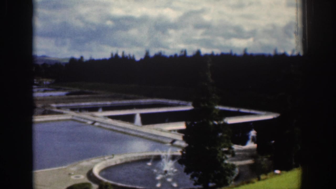 1961 Dublin footage showing concrete water basins, a circular pool, trees, hills, and a cloudy sky from a shaded vantage point.