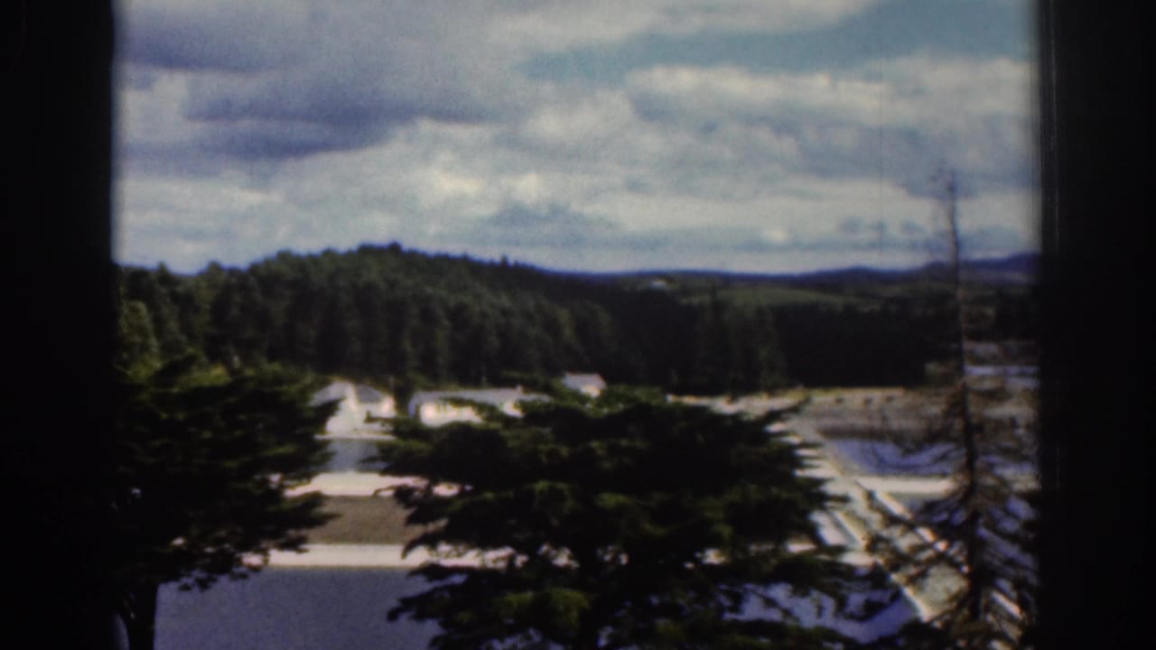 1961 Dublin, Ireland home-movie frame looking through a window toward wooded hills, pale roads or paths, and a clouded sky.