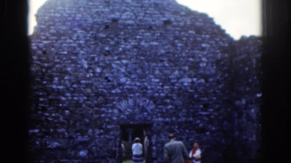 1961 Dublin home-movie frame showing adults near a weathered stone ruin with an arched doorway.