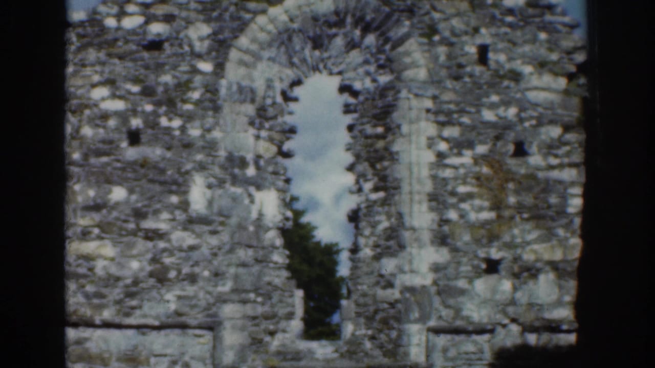 Weathered stone wall with a tall arched opening and cloudy sky beyond.