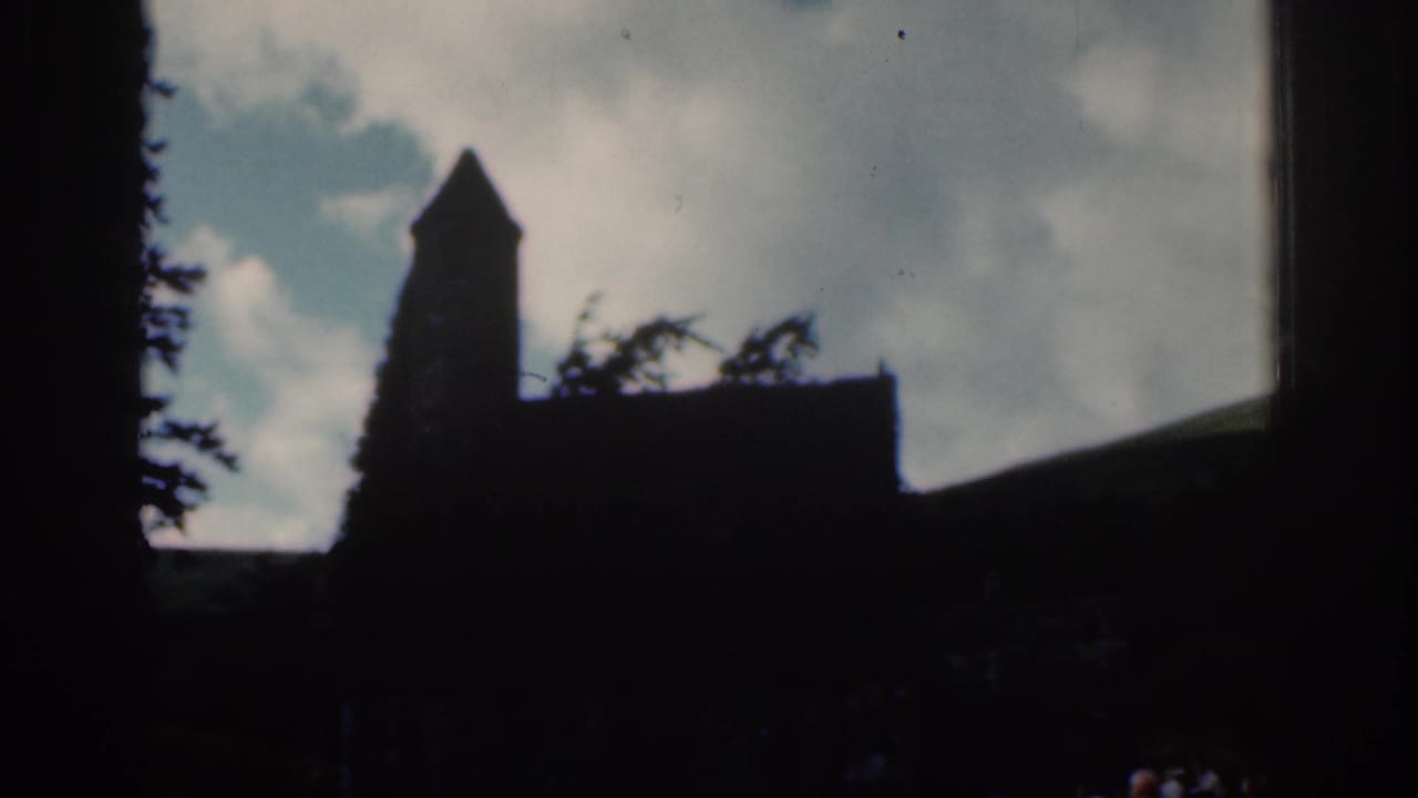 1961 Dublin-area 8mm frame with a silhouetted stone church tower, trees, hillside, and cloudy sky.