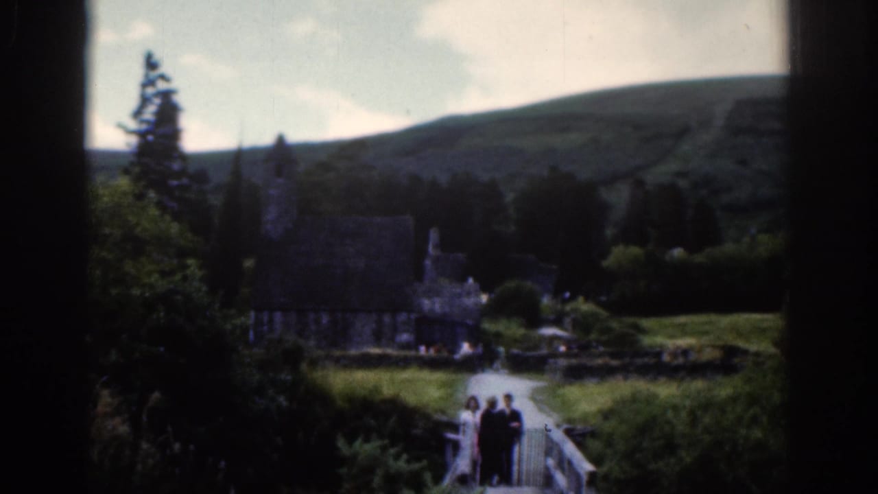 Stone church and tower in a green valley with visitors crossing a footbridge.