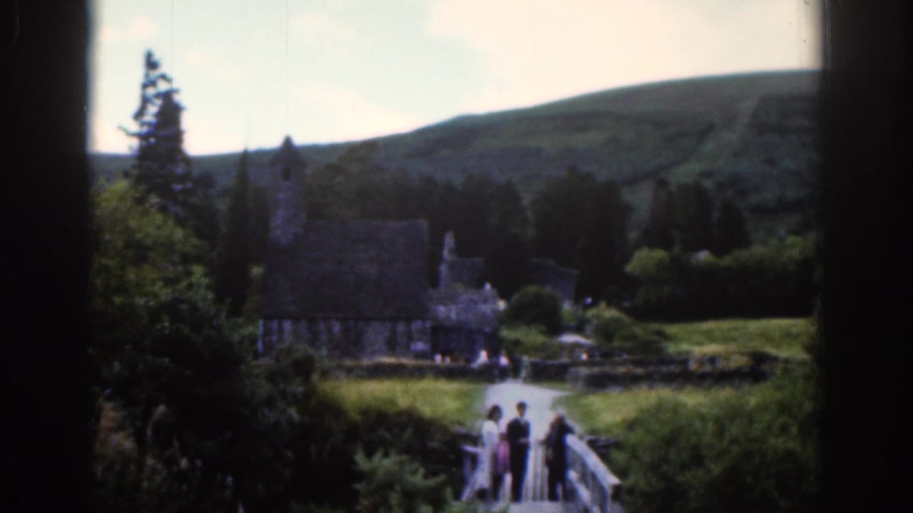 1961 Dublin-area home-movie frame showing visitors on a bridge with a stone church, trees, and hills beyond.