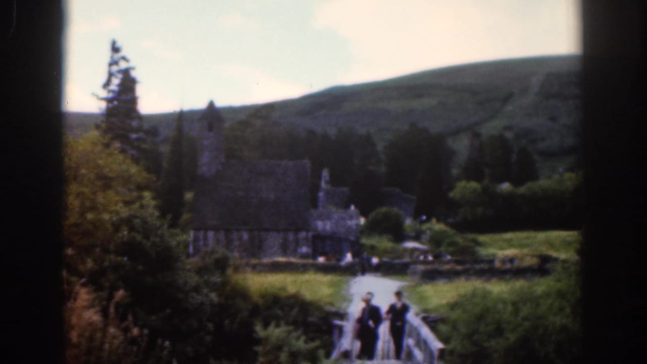 1961 Dublin-area 8mm frame with three visitors on a footbridge leading toward a stone church and hillside.